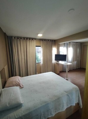 A hotel room with a bed, a TV, a small table, and curtains.