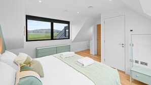 Et moderne soveværelse med en stor seng, udsigt over landskabet gennem et vindue, og et walk-in closet.