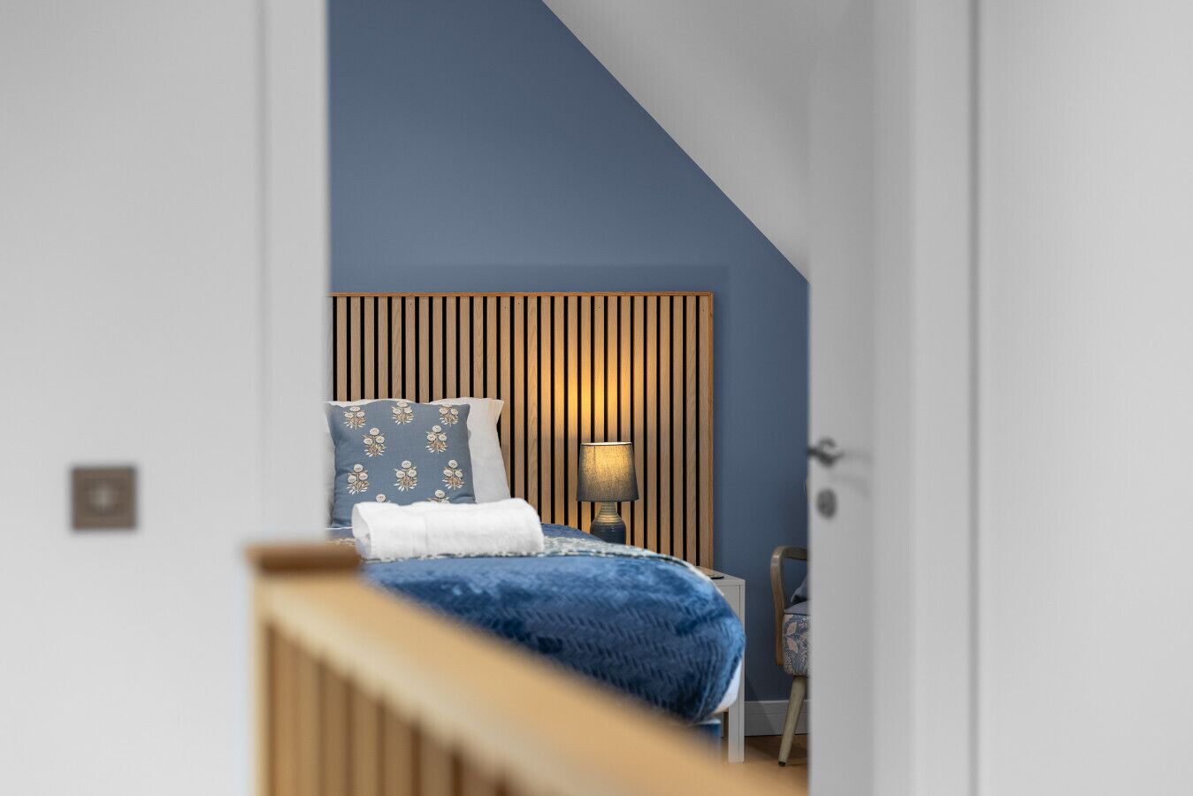 A bedroom with a bed, a nightstand, a lamp, and a wooden slat headboard.