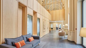 A modern hotel lobby with a grey sofa, wooden paneling, and a high ceiling. - Hôtel Maison Saint Charles (Paris)