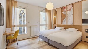 A modern hotel room with a large bed, a desk with a chair, a large window with curtains, and a painting on the wall. - Hôtel Maison Saint Charles (Paris)