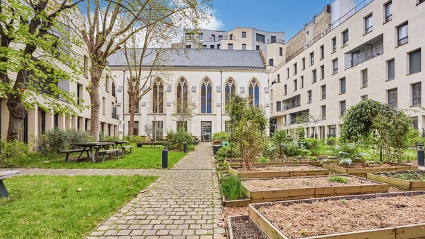 A courtyard with a brick pathway, wooden raised garden beds, and a building with arched windows and balconies. - Hôtel Maison Saint Charles (Paris)