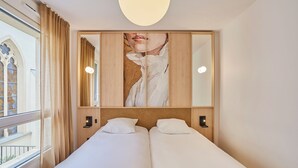 A hotel room with a large bed, a painting above the bed, and a window with curtains. - Hôtel Maison Saint Charles (Paris)