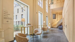 A spacious hotel corridor with modern chairs, a staircase, and a sign indicating amenities like a gym and a restaurant. - Hôtel Maison Saint Charles (Paris)