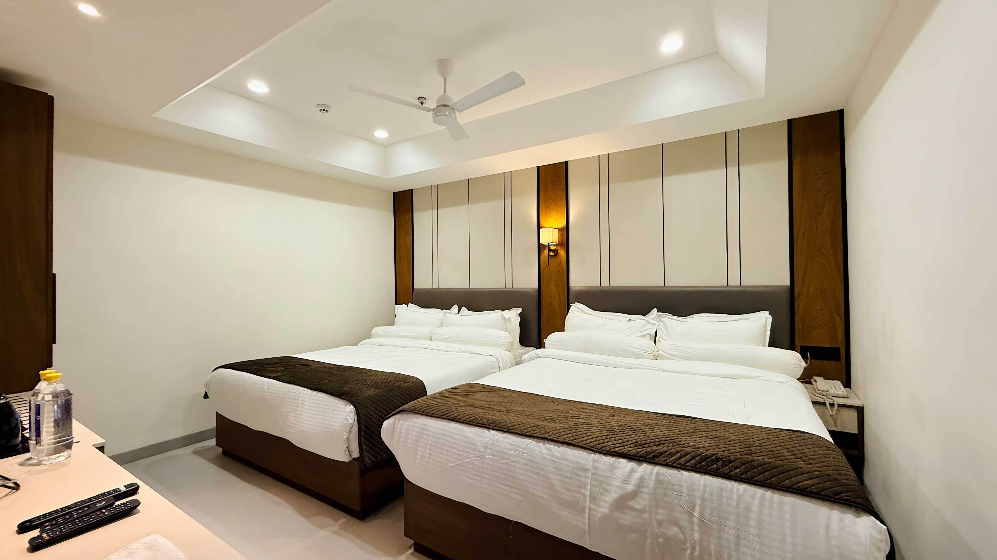 A hotel room with two beds, a ceiling fan, recessed lighting, and a bedside table with a phone and a bottle.