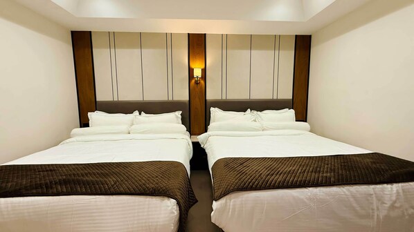 Habitación de hotel con dos camas, cabecera de madera y una lámpara fijada a la pared.