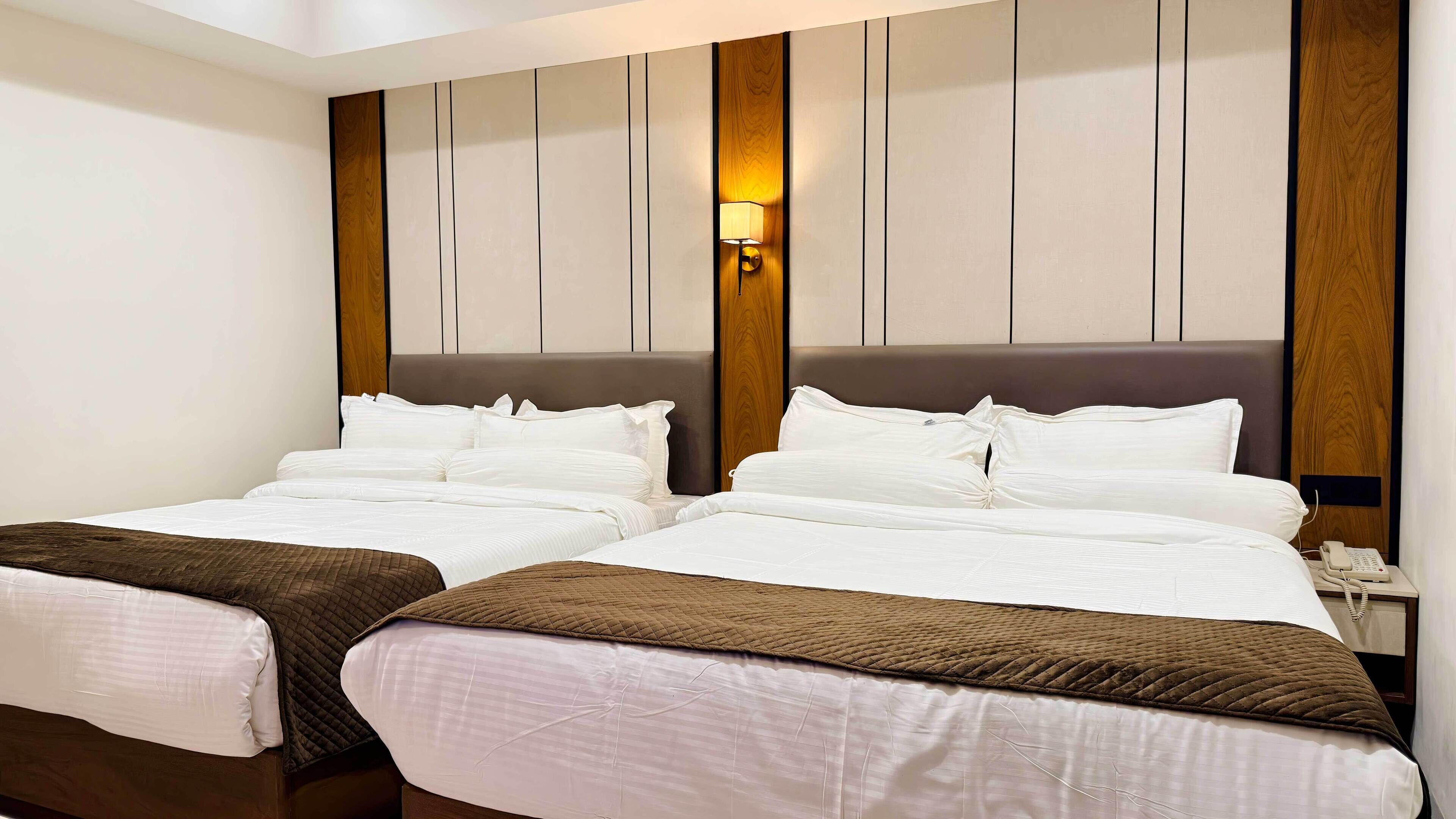 Una habitación de hotel con dos camas, cabecero de madera, lámpara de pared y teléfono en la mesita de noche.