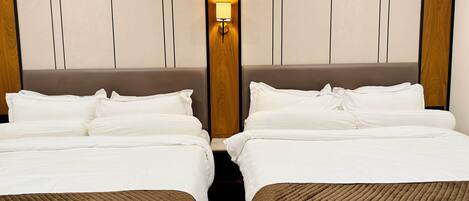 Una habitación de hotel con dos camas, cabecero de madera y mesita de noche fijada a la pared.