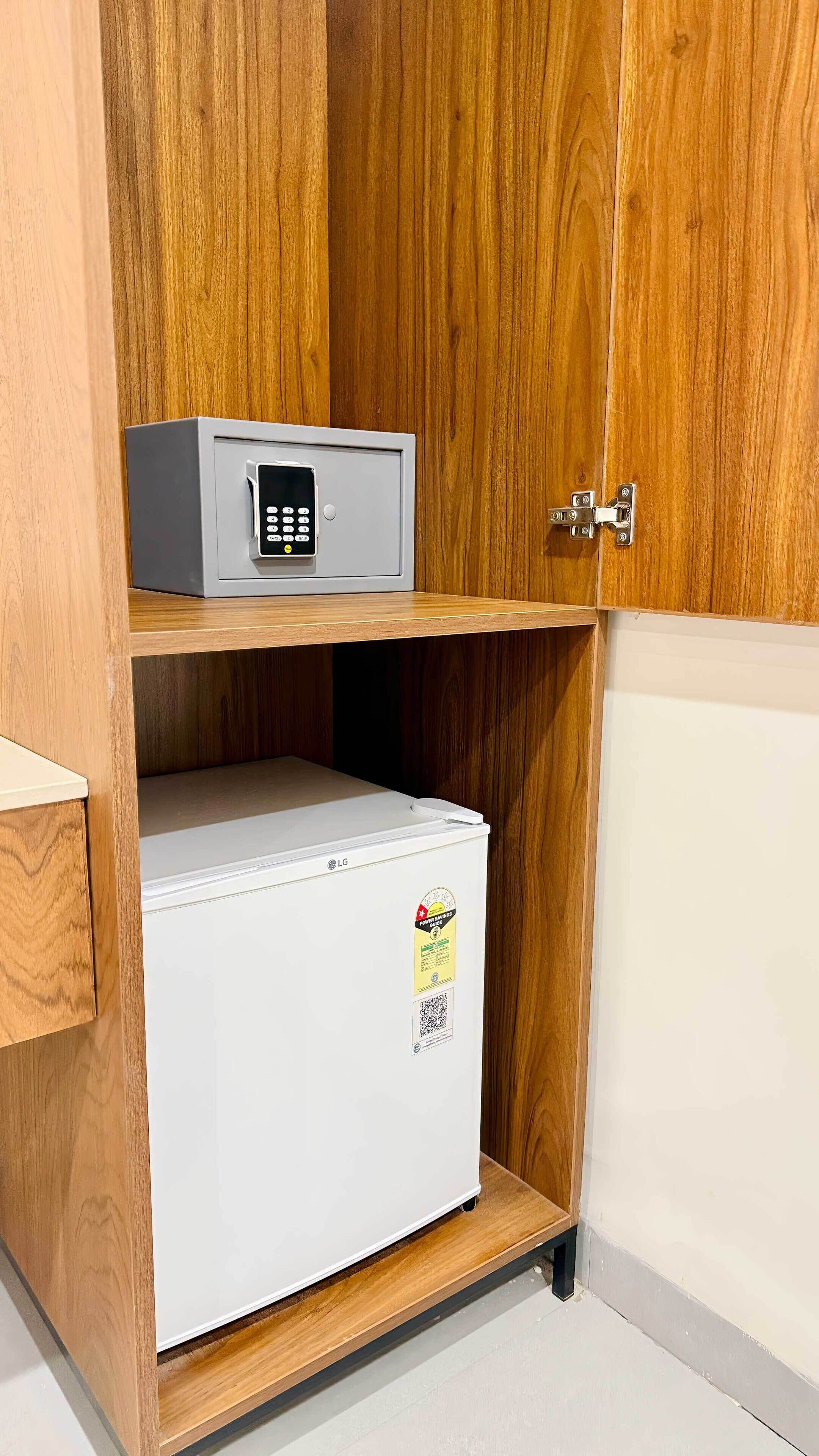 A wooden cabinet with a white LG refrigerator and a digital safe on the top shelf.