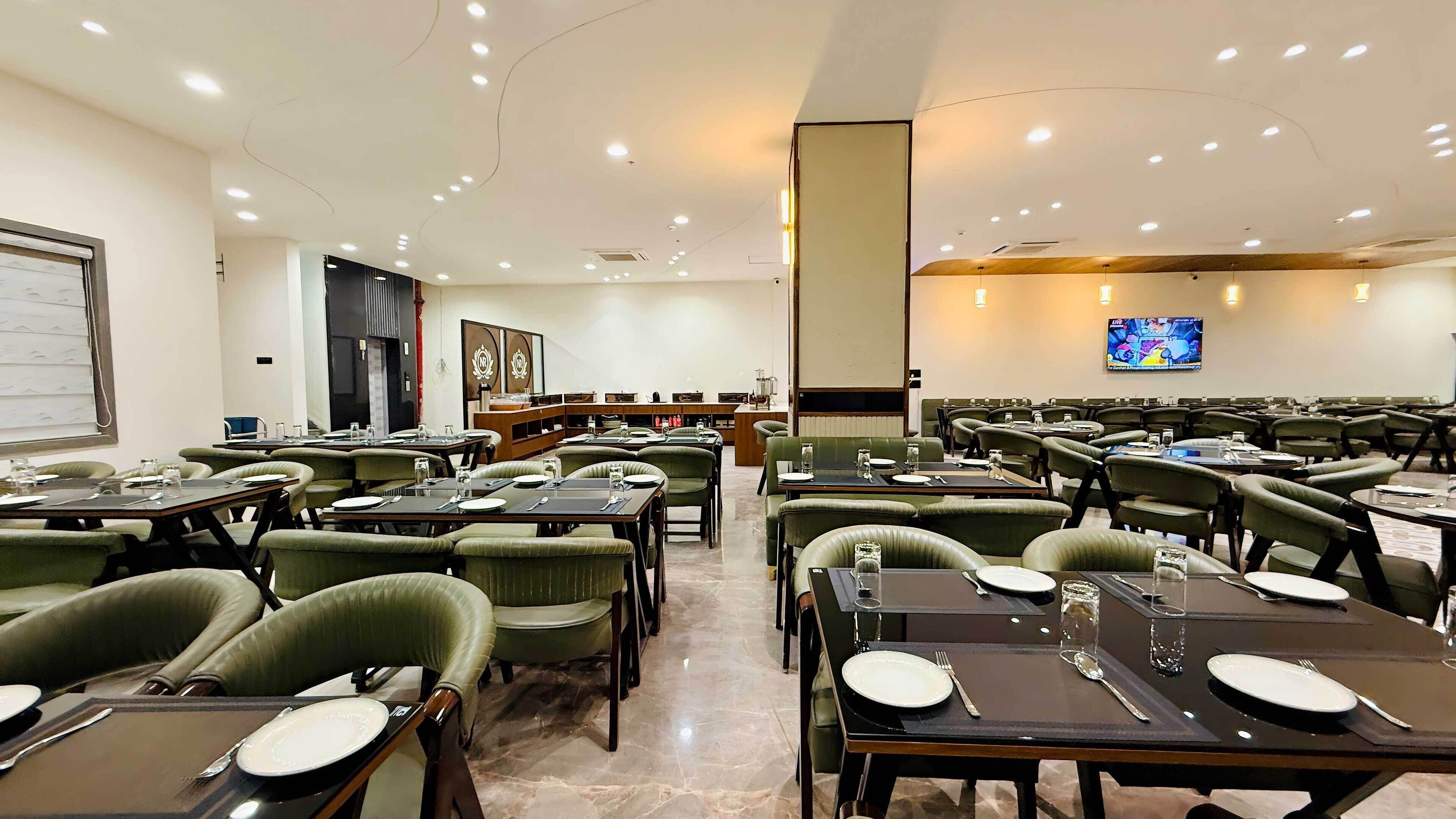 A spacious dining area with multiple tables and chairs, a large screen on the wall, and a reception desk in the background.