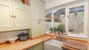 Una cucina con mobili verdi, un piano di lavoro in legno, un lavello e una finestra con vista su un muro di mattoni e piante.