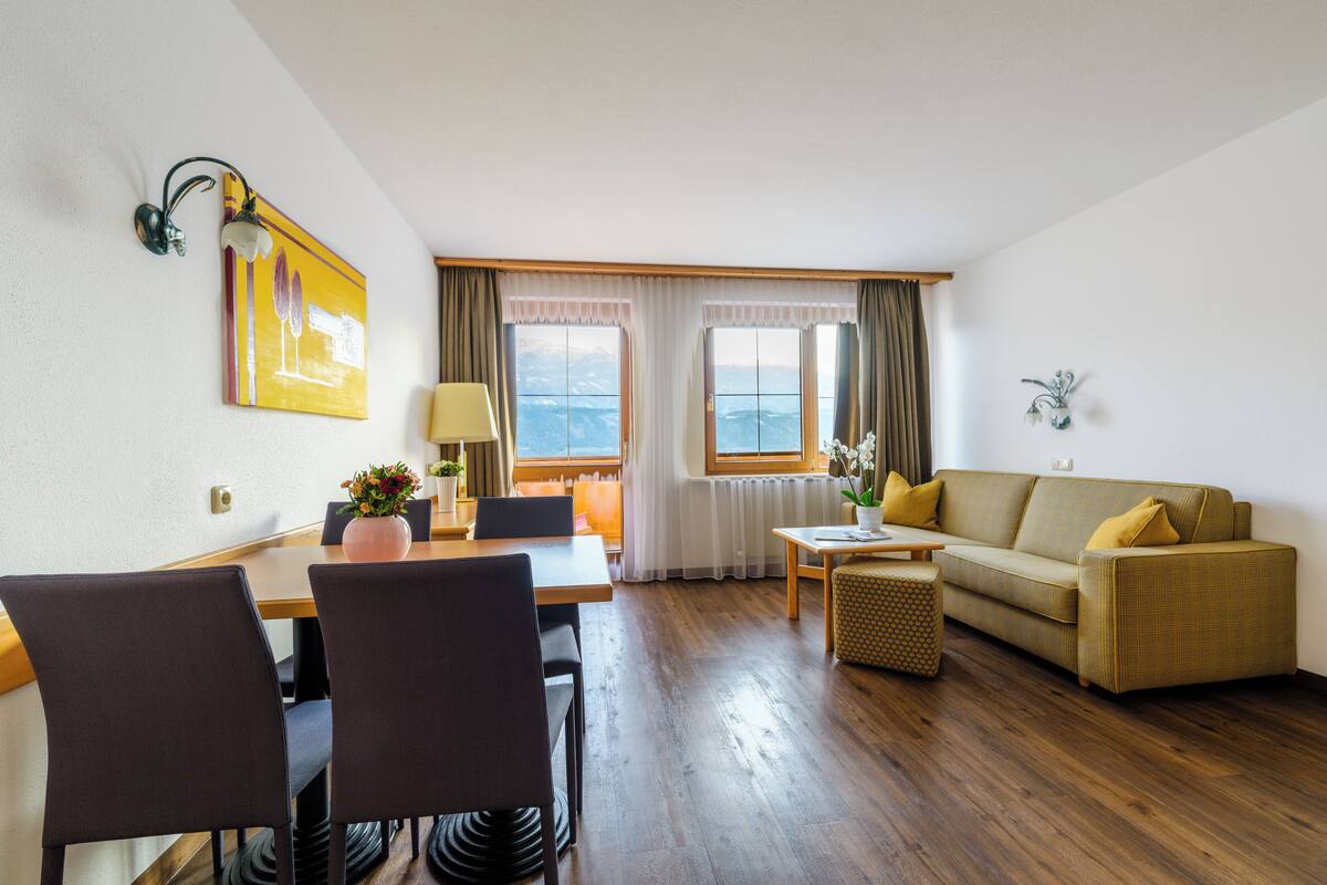 Una habitación con una mesa de comedor, sillas, un sofá y una ventana con cortinas.