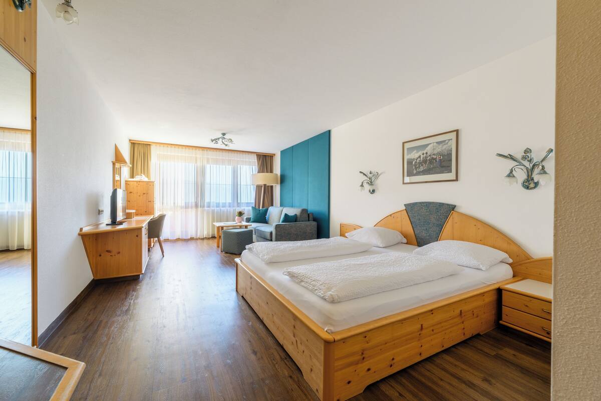 Una habitación de hotel con una cama de madera, un escritorio con lámpara, un sofá y una ventana con cortinas.