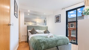 A modern bedroom with a bed, a mirror, and a view of the outside. - Long stay | 1-Bed Jewellery Quarter Apt | Homely (Birmingham)