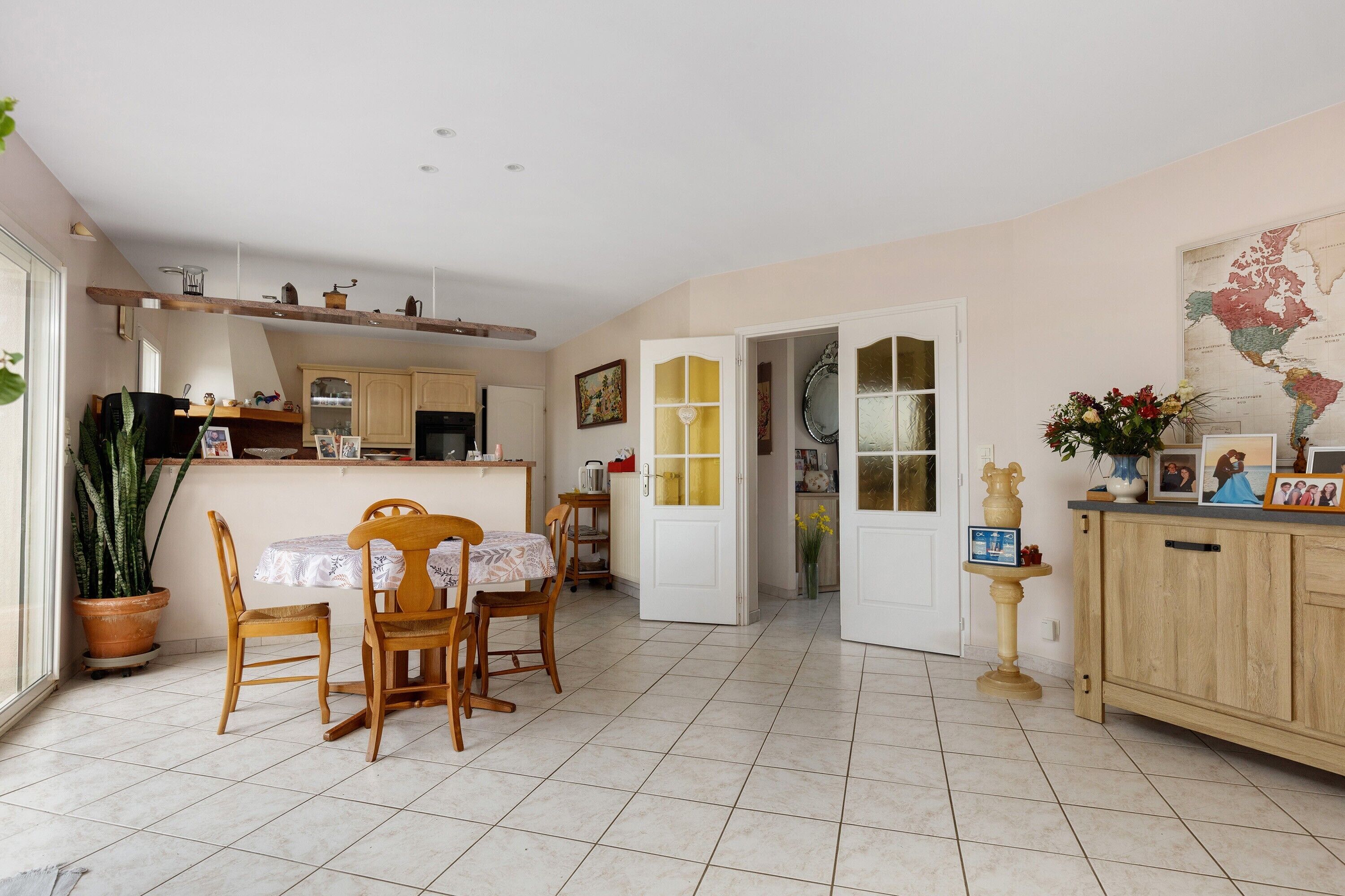 Une cuisine avec des meubles en bois, une table à manger avec des chaises, une plante en pot et une carte accrochée au mur.