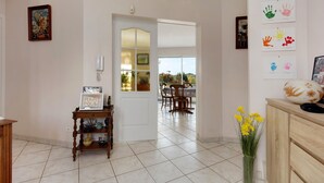Quarto com porta de madeira, uma pequena mesa com um quadro emoldurado, um vaso com flores amarelas e uma parede com decorações de mão.