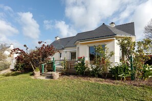 Une maison d’habitation avec un toit en pente, un porche à l’avant et un jardin bien entretenu.