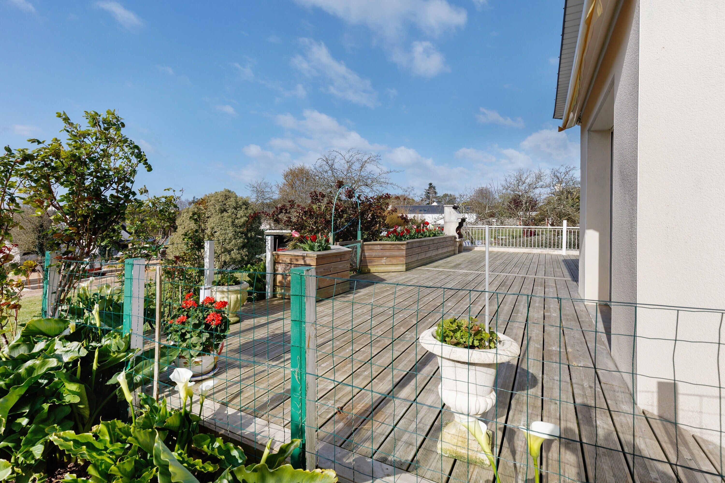 A rooftop garden with wooden decking, potted plants, and a metal fence.