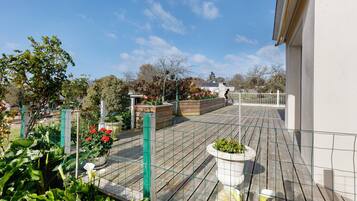 A rooftop garden with wooden decking, potted plants, and a metal fence.