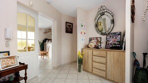 Quarto com um armário de madeira, um espelho, um vaso com flores, um quadro em uma mesa e uma porta que dá para outro quarto.