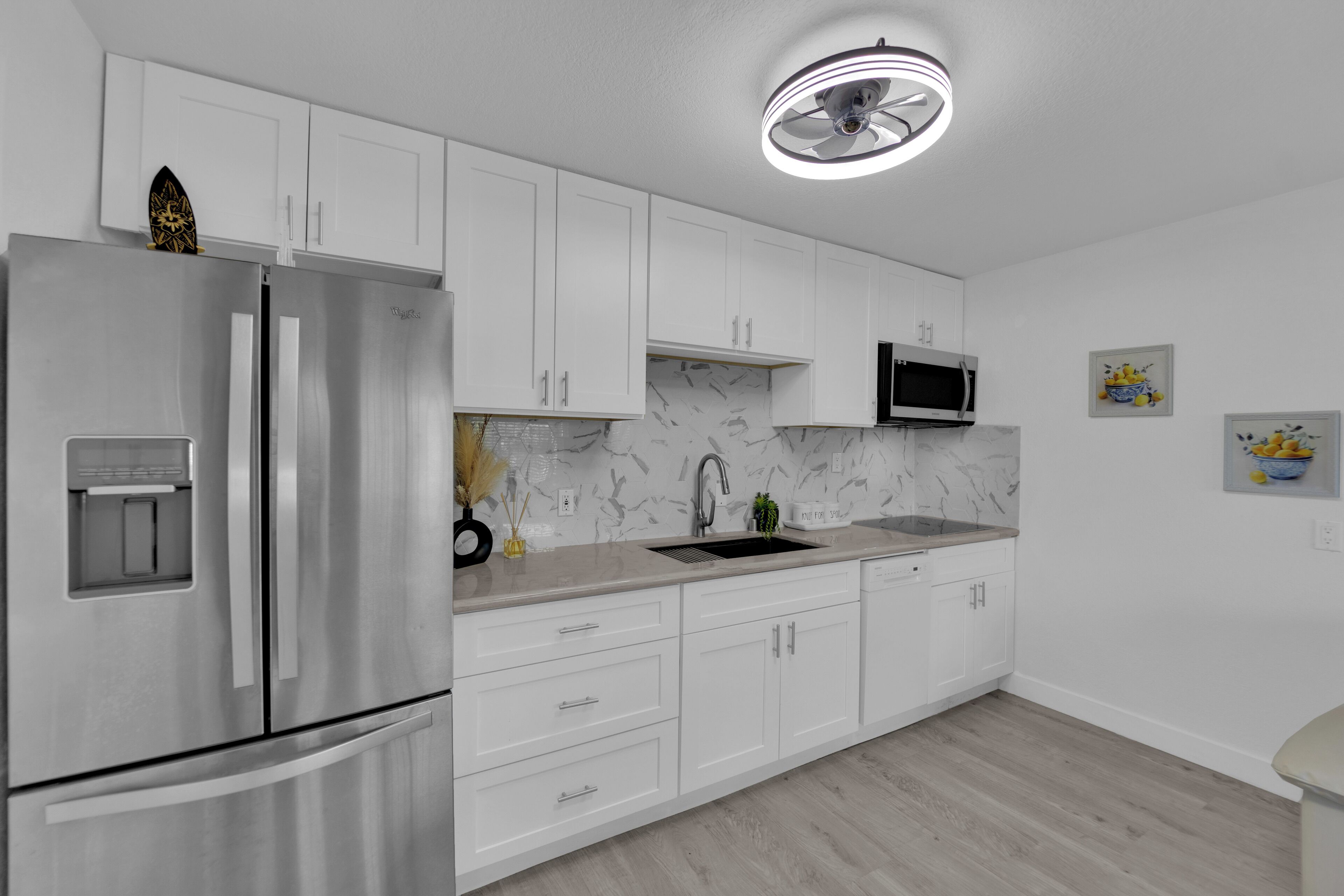 A modern kitchen with white cabinets, a stainless steel refrigerator, a microwave, and a sink.