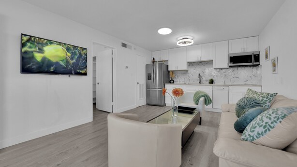 A modern kitchen with white cabinets, a stainless steel refrigerator, and a microwave. There is a dining area with a glass table and a beige sofa. - Cozy 1-bedroom condo walking distance to Las Vegas strip (Las Vegas)