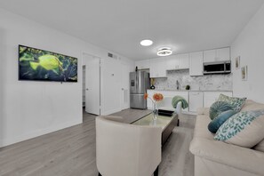 A modern kitchen with white cabinets, a stainless steel refrigerator, and a microwave. There is a dining area with a glass table and a beige sofa. - Cozy 1-bedroom condo walking distance to Las Vegas strip (Las Vegas)