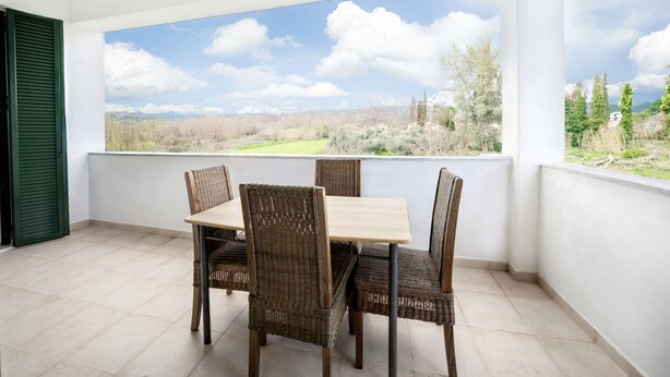 Ein Balkon mit Tisch und Stühlen, mit Blick auf eine Landschaft aus Bäumen und Bergen.