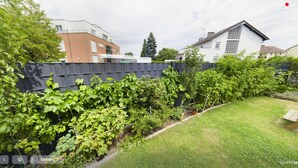Un jardín con parras, una terraza de madera y un césped.