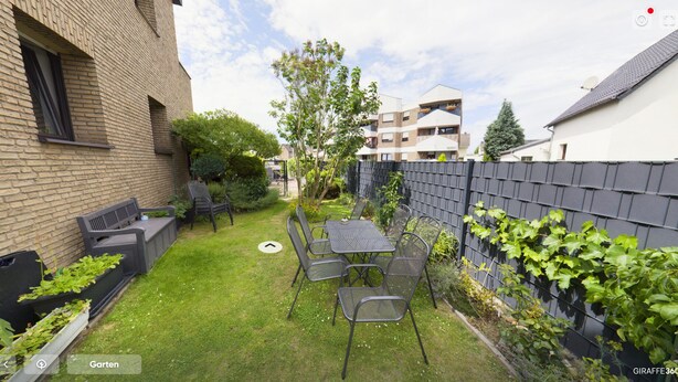 Un jardín cuidado con una mesa y sillas, un muro de ladrillo y una valla.