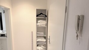 Una habitación limpia y moderna con piso de madera, un felpudo negro, un armario blanco con ropa doblada y un teléfono montado en la pared.