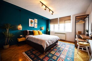 Ein modernes Schlafzimmer mit einer Türkis-farbenen Akzentwand, einem großen Bett, einem Schreibtisch mit Stuhl und einem Fenster mit Jalousien.