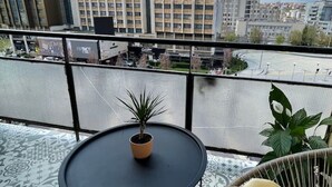 A balcony with a round table, a potted plant, and a wicker chair with a cushion. - Cozy Bright Central APT (Prishtina)