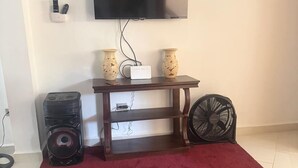 Ein Wohnzimmer mit Fernseher, zwei Lautsprechern, einem Ventilator und einem roten Teppich.