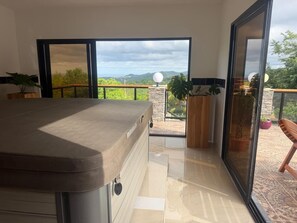 A modern room with a large window, a hot tub, and a view of greenery.