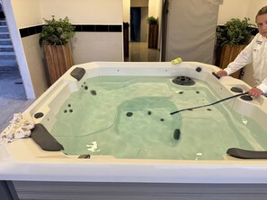 Ein Whirlpool mit einer Person, die ein langes Werkzeug benutzt, umgeben von Holzkästen und einer gefliesten Wand.