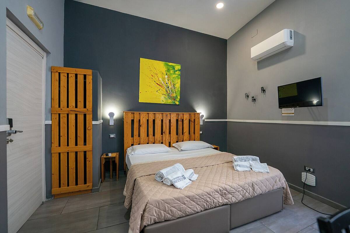 A bedroom with a bed, a wooden headboard, a wall-mounted TV, and an air conditioning unit.