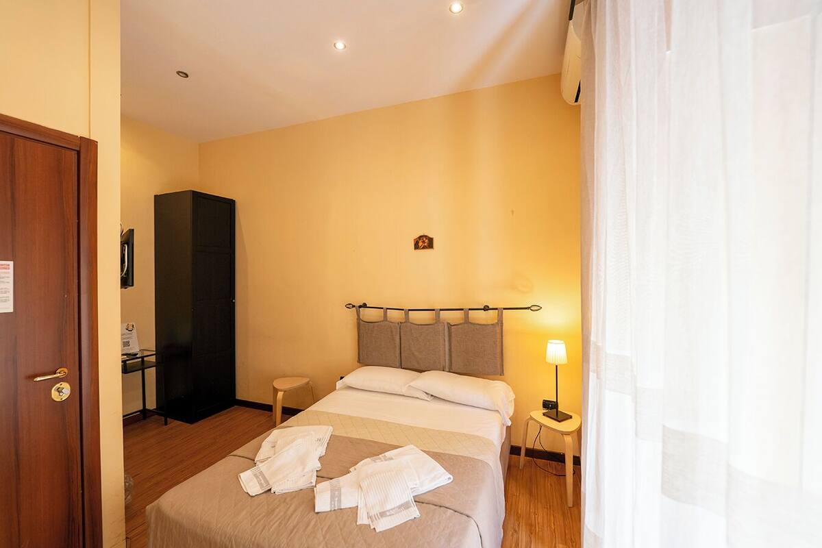 A hotel room with a bed, a desk, a wardrobe, and a lamp.