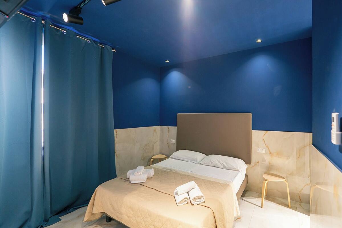 A hotel room with a bed, a nightstand, a chair, and a curtain.