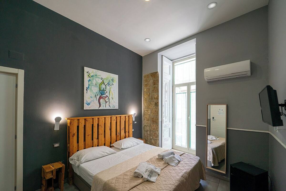 A bedroom with a wooden bed, a painting on the wall, a window, and a TV.