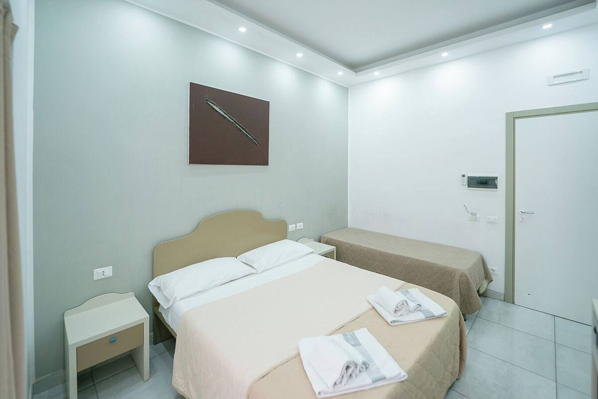 A hotel room with two beds, a nightstand, a wall clock, and a door.