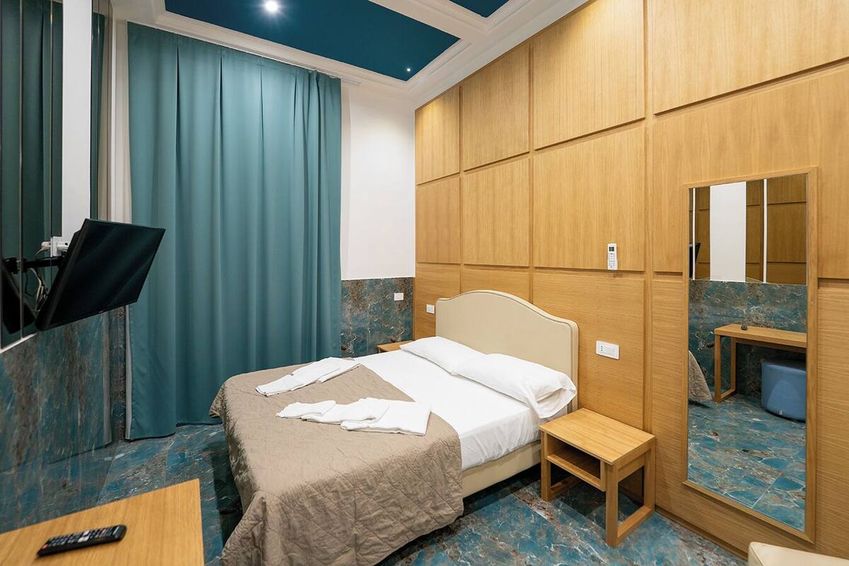 A hotel room with a bed, a TV, a desk, and a mirror.