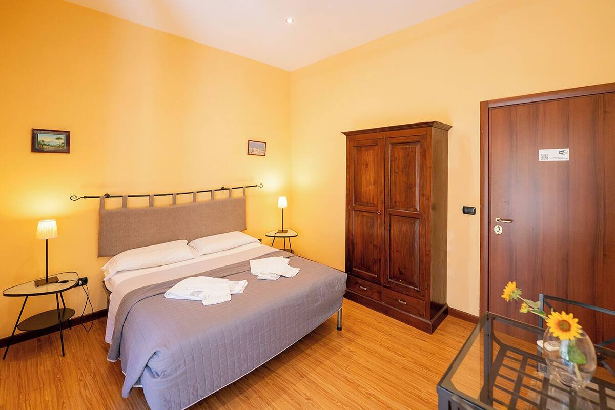 A hotel room with a bed, bedside tables, a wardrobe, and a door.