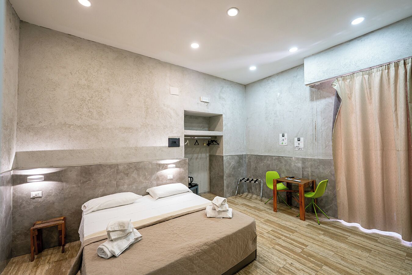 A hotel room with a large bed, a small table, two chairs, a shower area, and a curtain.