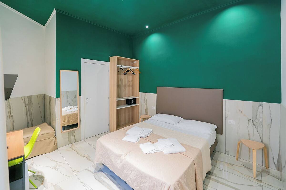 A modern bedroom with a bed, a wardrobe, a small stool, and a mirror.