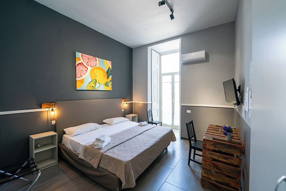 A modern bedroom with a large bed, bedside tables, a desk with a chair, and a colorful painting on the wall.