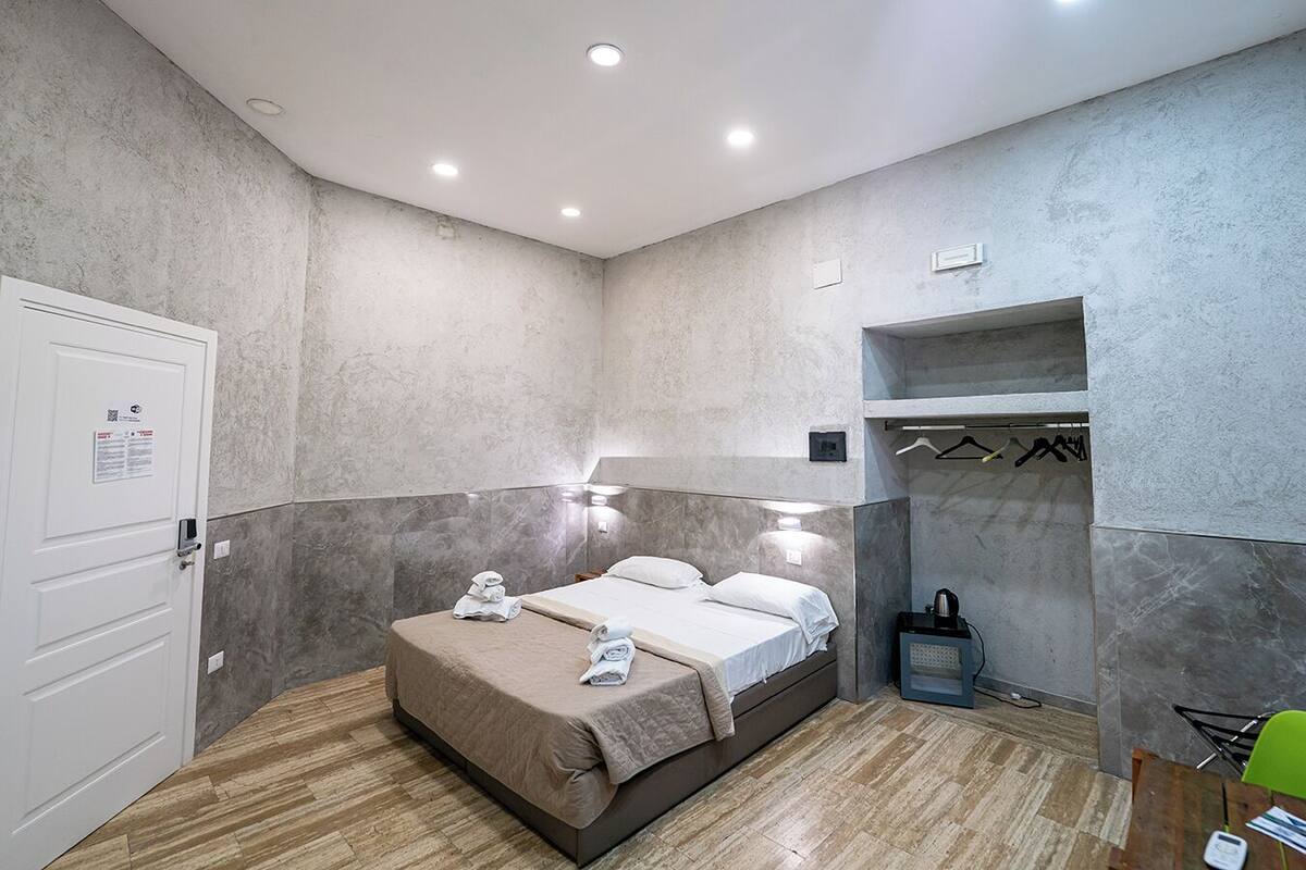 A modern hotel room with a bed, a seating area, and a coat rack.