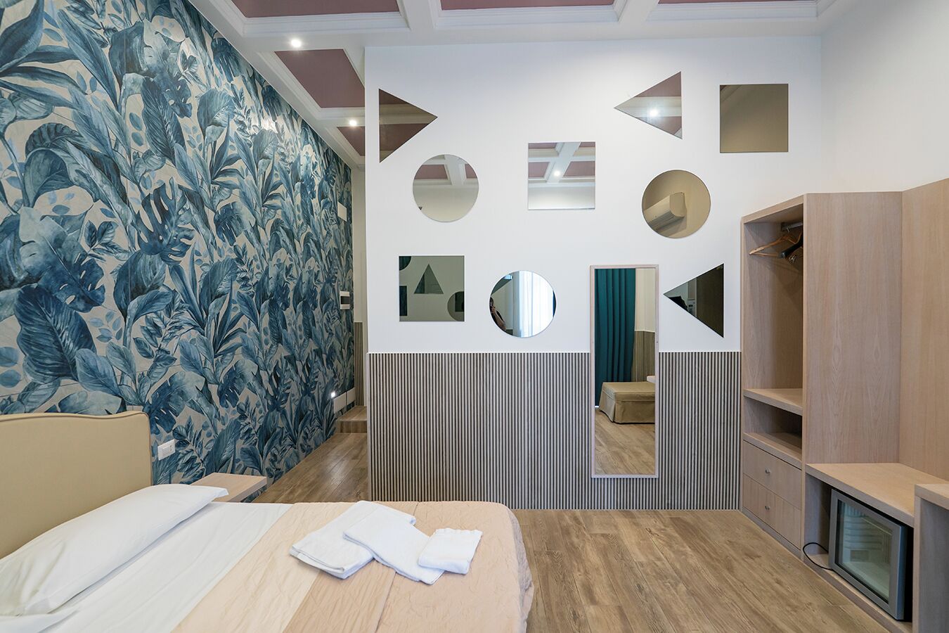 A modern hotel room with a bed, a mirror, and a wardrobe.