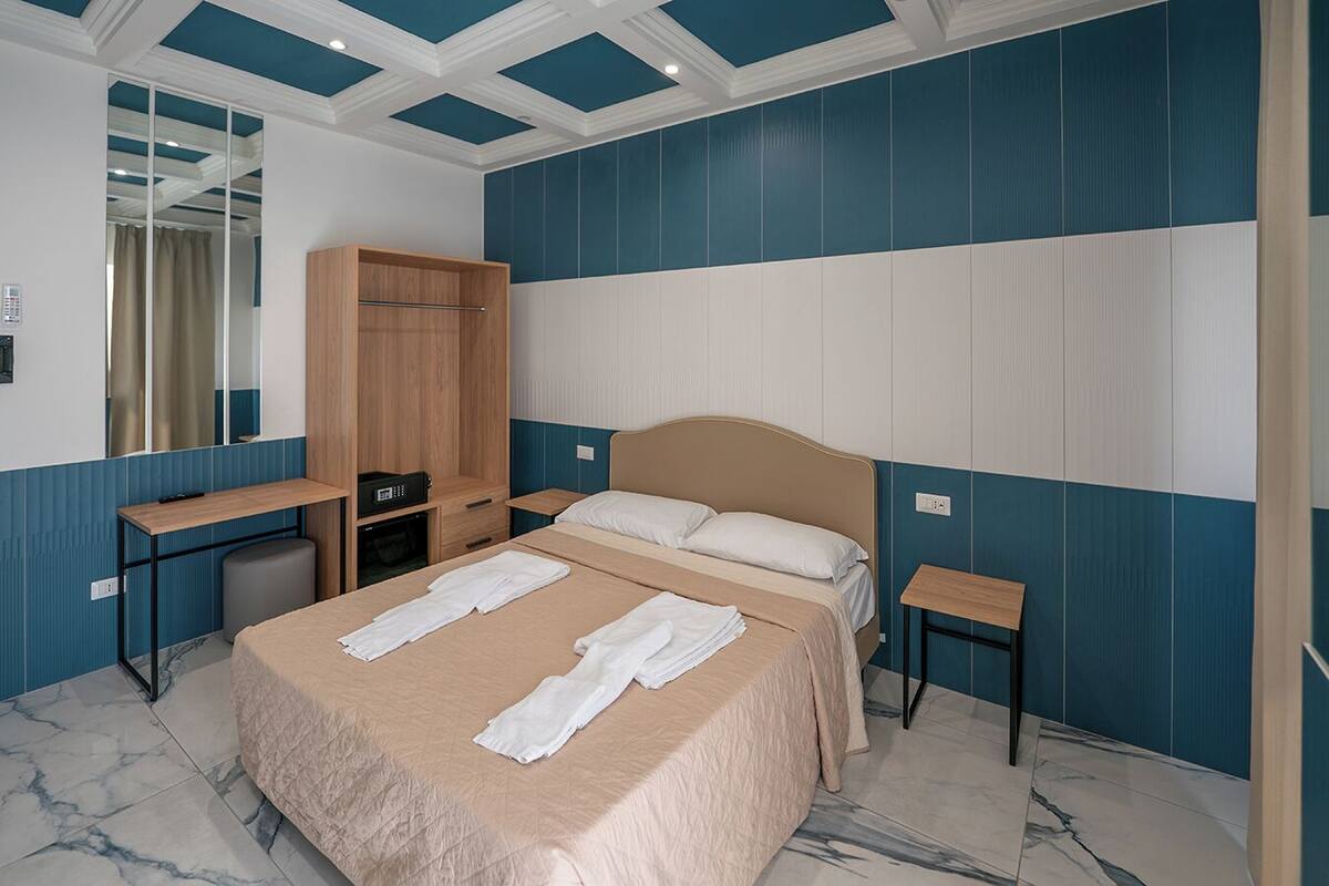 A hotel room with a bed, a desk, a wardrobe, and a mirror.