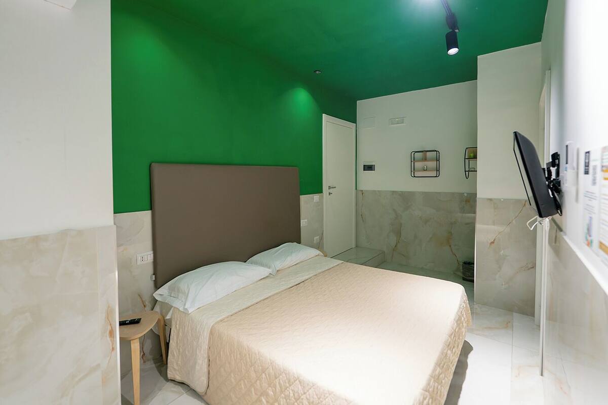 A hotel room with a bed, a small table, a mirror, and a shower area.